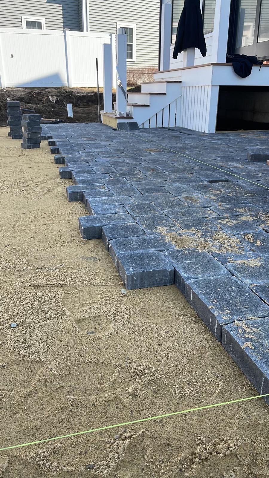 Charcoal paver patio installation in progress, showing precise herringbone bond